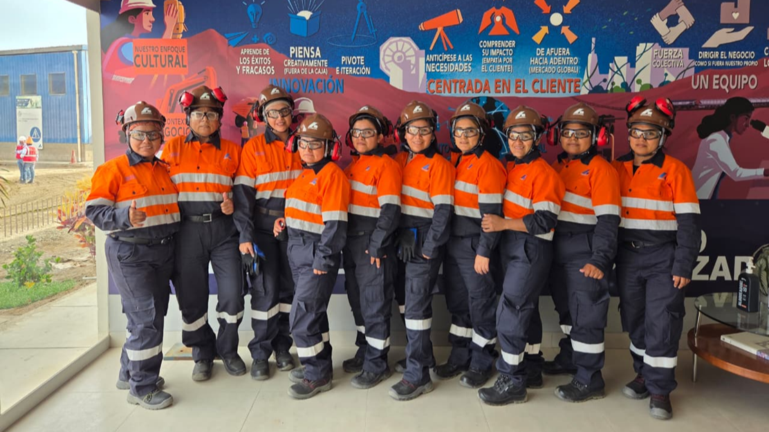 10 women in orange and blue high-vis work uniforms and hard hats, stand together in a line